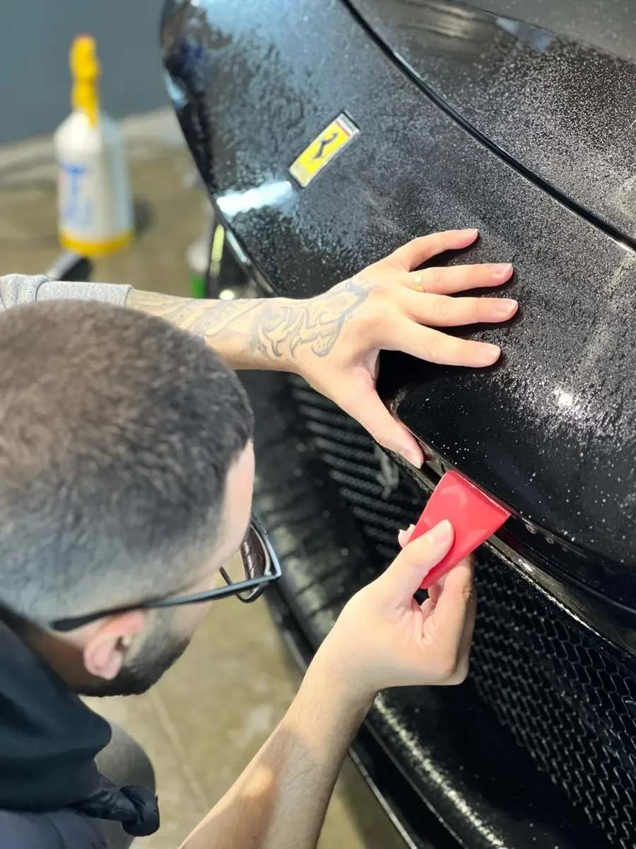 Instalador aplicando PPF na frente de um carro preto